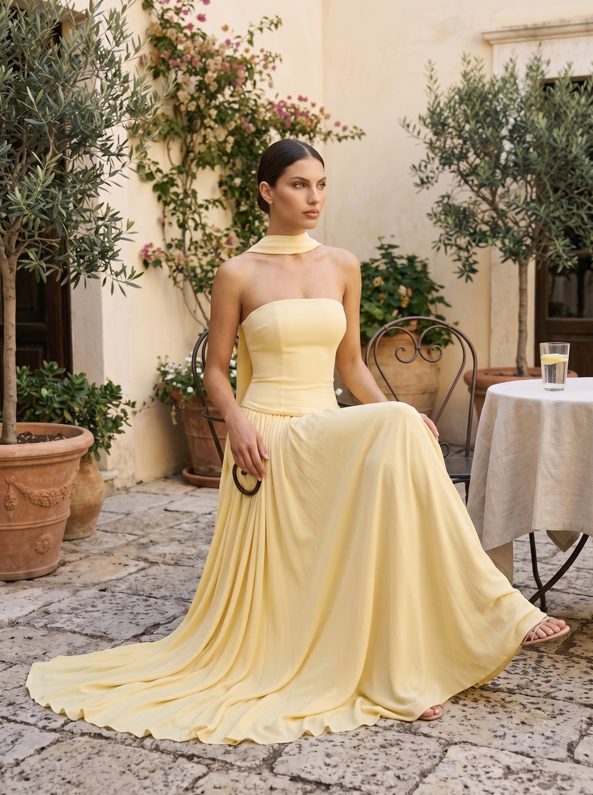 Vestido largo amarillo Vezza, mujer sentada en patio mediterráneo, look de ceremonia